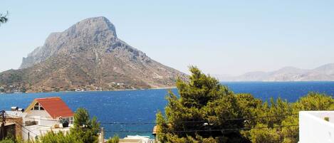 A coastal view with a prominent mountain, a clear blue sea, and residential buildings with red roofs.