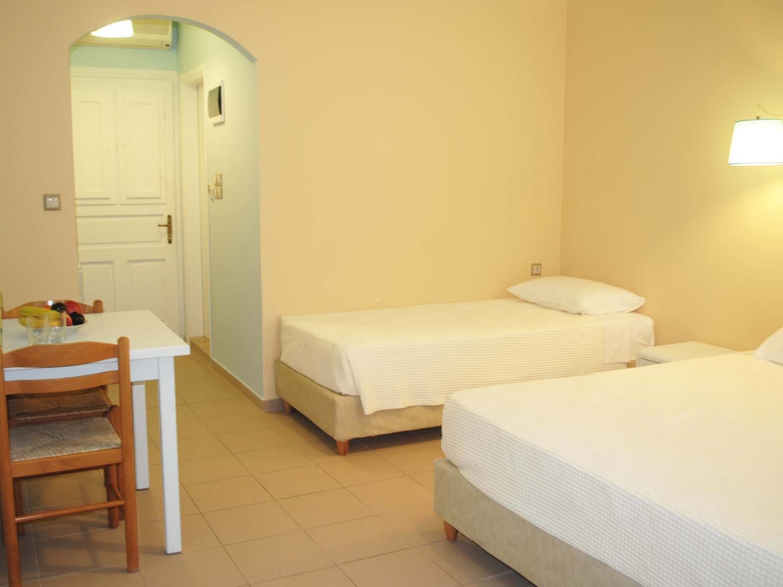 A small, clean room with two single beds, a table with chairs, and a door leading to another room.