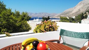 Una mesa con un plato de fruta y una silla con vistas a un paisaje montañoso y al mar.