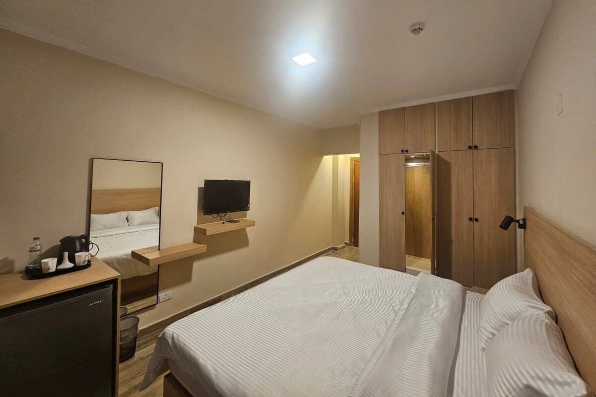 Una habitación de hotel con una cama, un escritorio con televisor, un espejo y un armario.