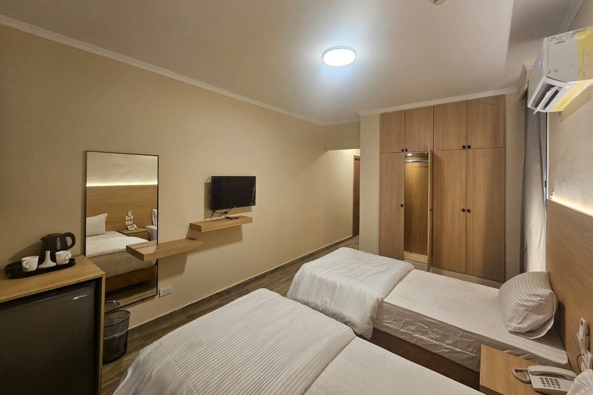 Habitación de hotel con dos camas, un escritorio con cafetera, televisión y armario.