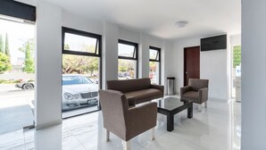 A modern lobby with a sofa, armchair, and coffee table. Large windows offer views of the street. - Suites Internacional (Zapopan)