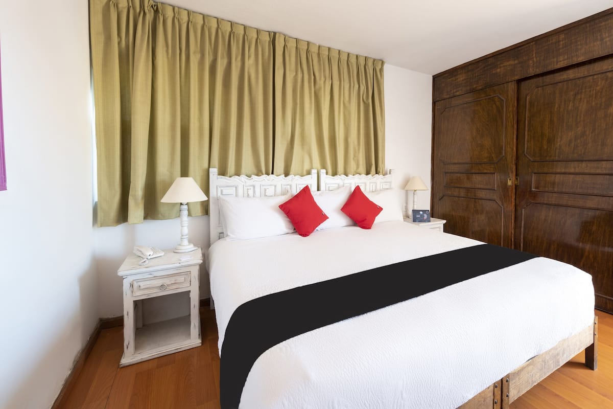 Habitación de hotel ordenada con una cama grande, dos mesitas de noche, un armario de madera y una cortina verde.