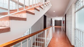 A staircase with white railings and a wooden handrail, leading to a hallway with patterned floor tiles and a fire extinguisher mounted on the wall. - Suites Internacional (Zapopan)