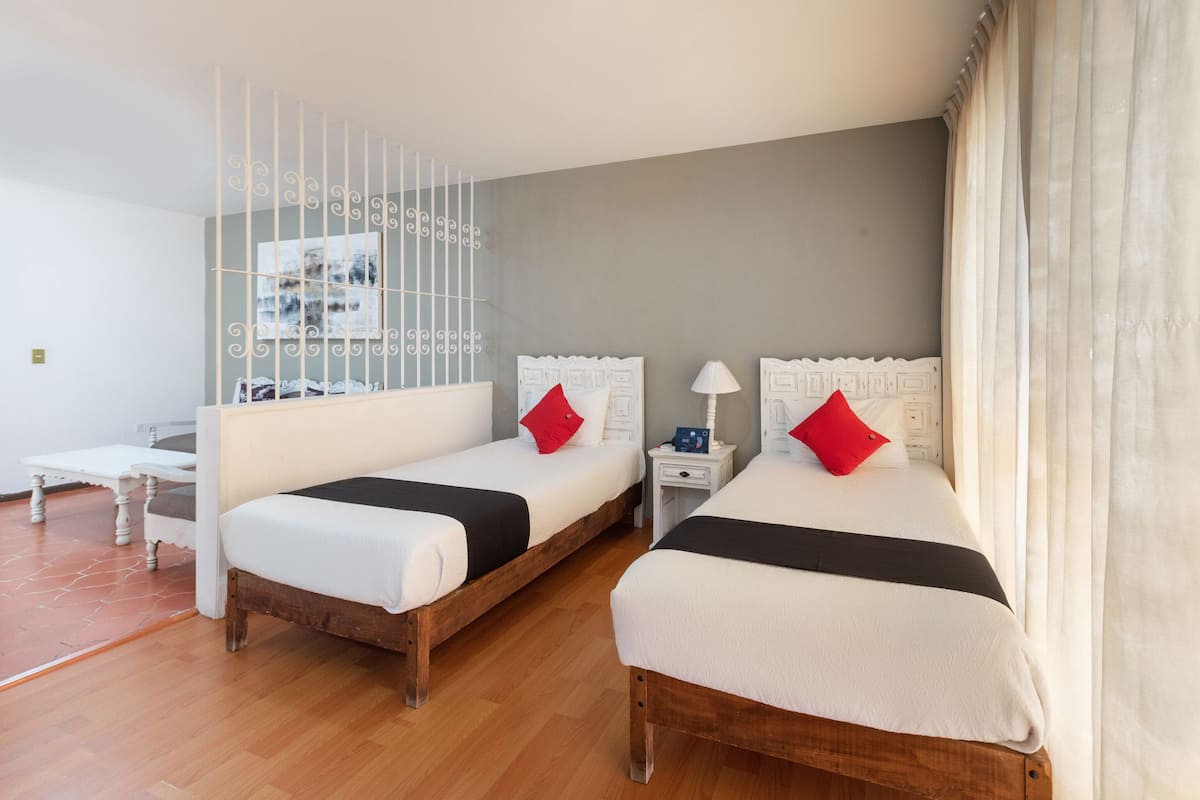 Una habitación de hotel moderna con dos camas individuales, una mesita de noche pequeña con lámpara y suelo de madera.