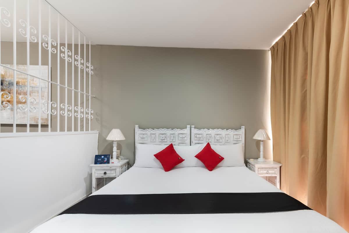 Un dormitorio ordenado con cama, dos mesitas de noche y un aparador.