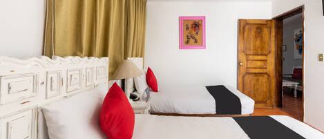 Habitación de hotel con dos camas, una puerta de madera, un cabecero blanco, una lámpara y un cuadro en la pared.
