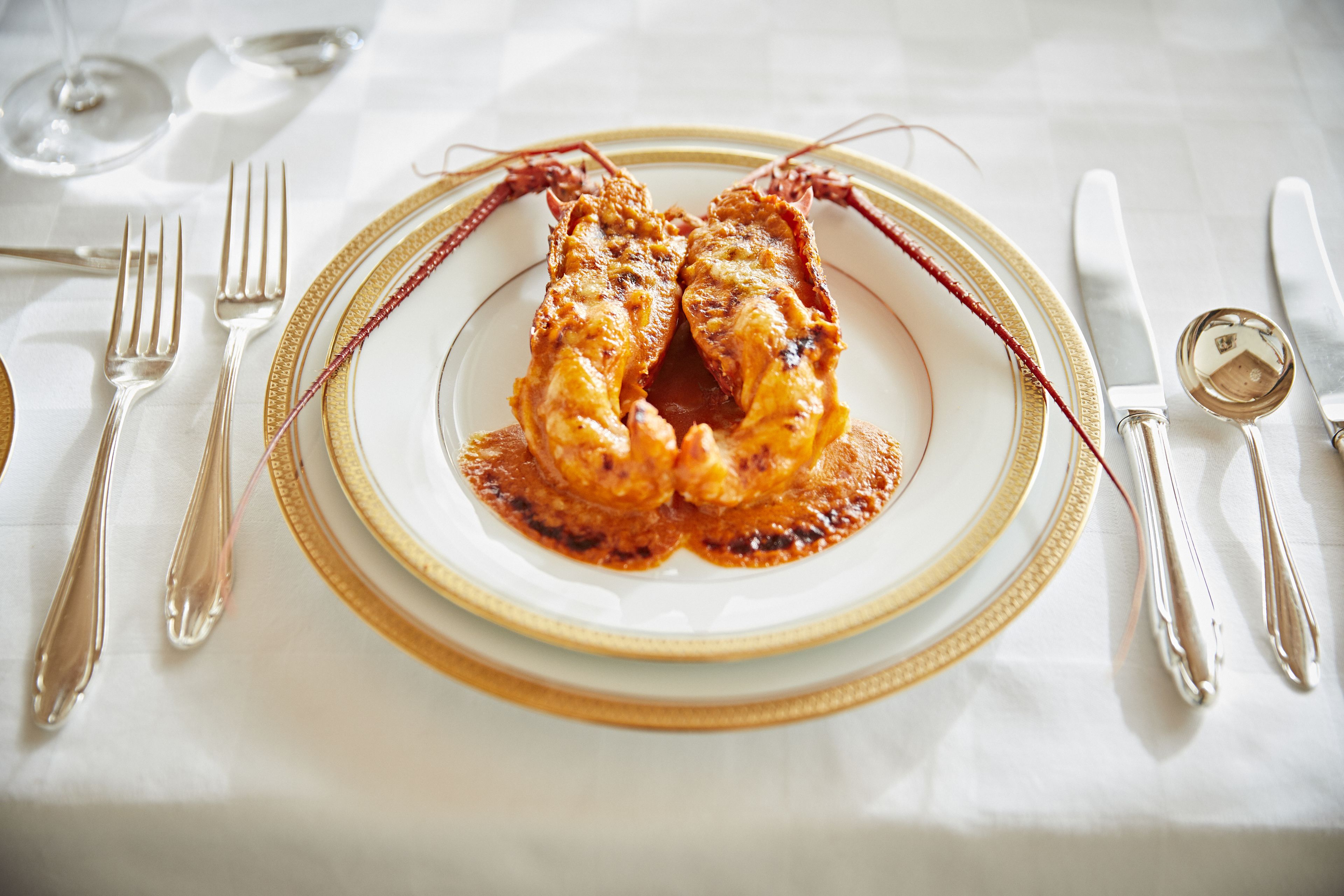 A formal dining table set with a white tablecloth, gold-rimmed plates, and silverware.