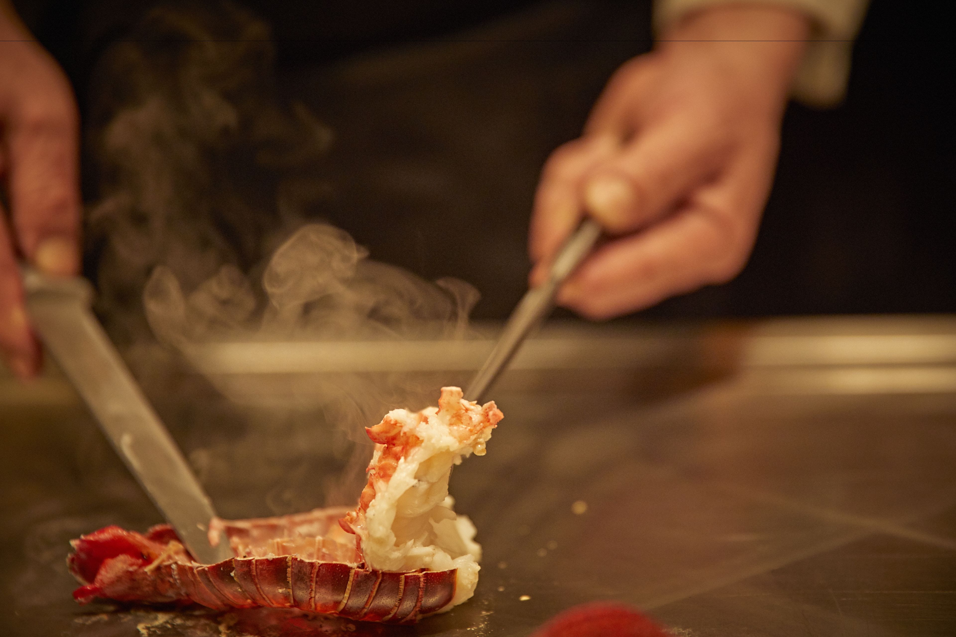 A person cutting a lobster on a table.