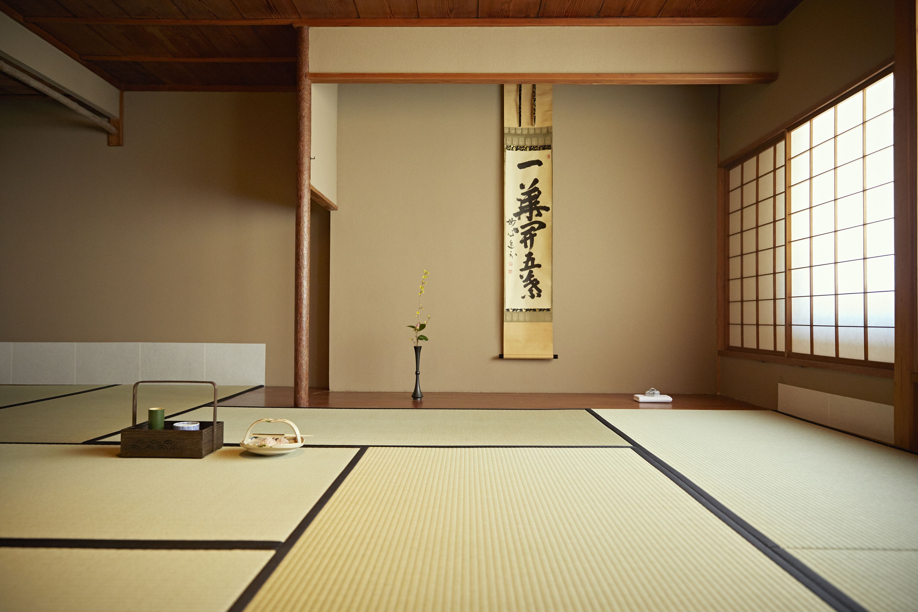 A tatami mat room with a shoji screen, a hanging scroll, and traditional Japanese furniture.