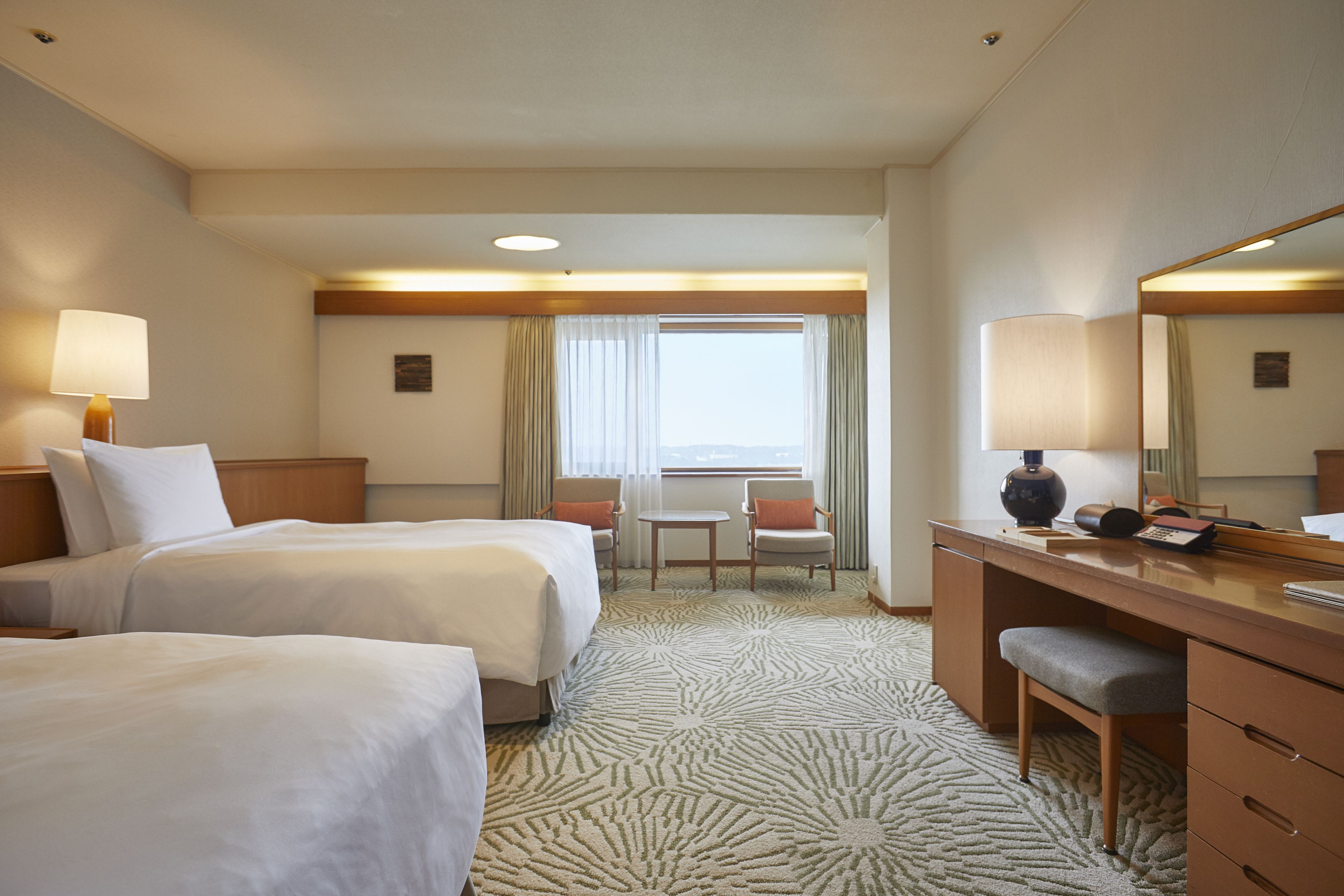 Ein Hotelzimmer mit zwei Betten, einem Schreibtisch, einem Stuhl, einem kleinen Tisch und einem großen Spiegel.
