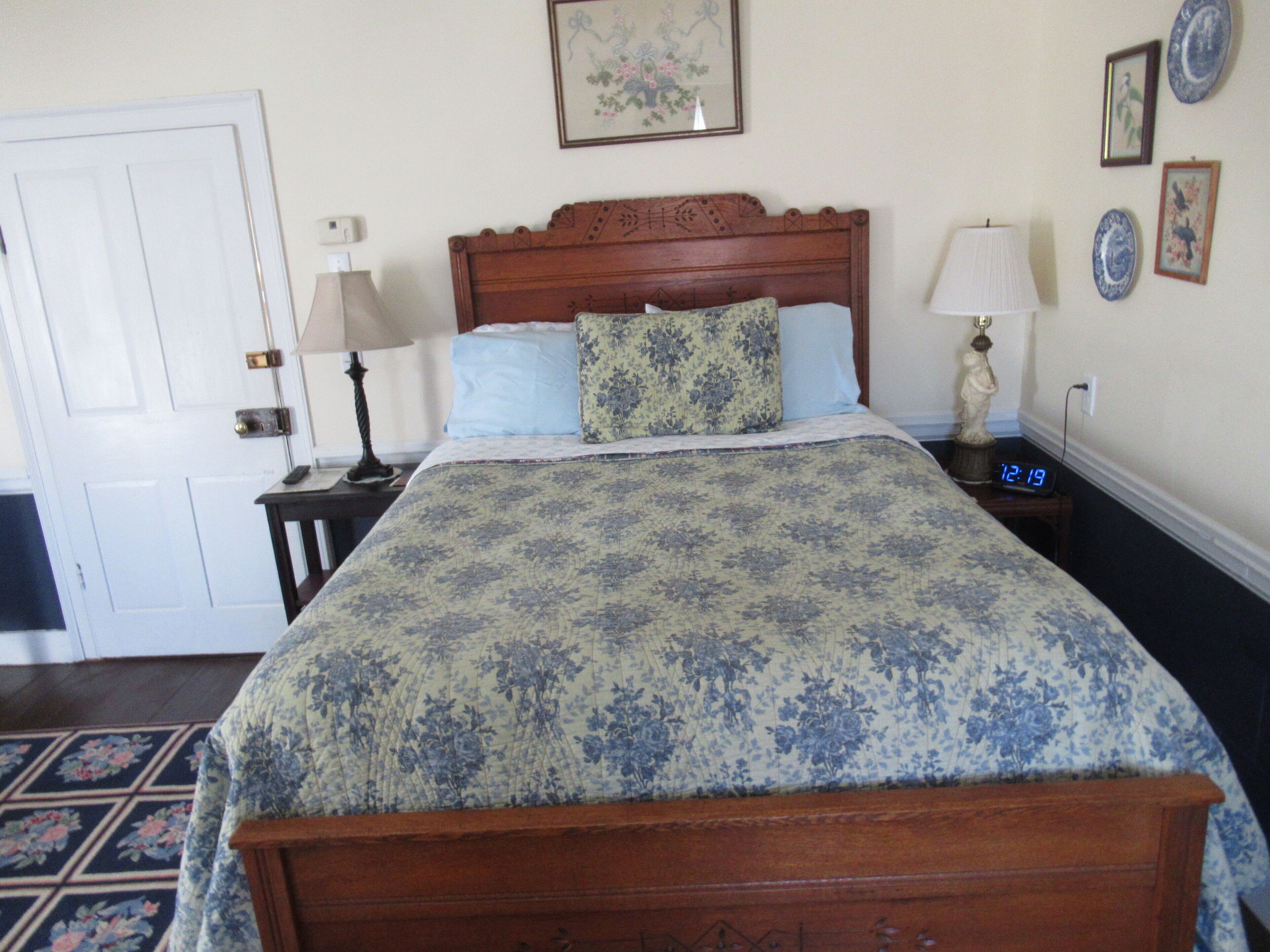 A neatly made bed with floral bedding, a wooden headboard, bedside lamps, and a clock.