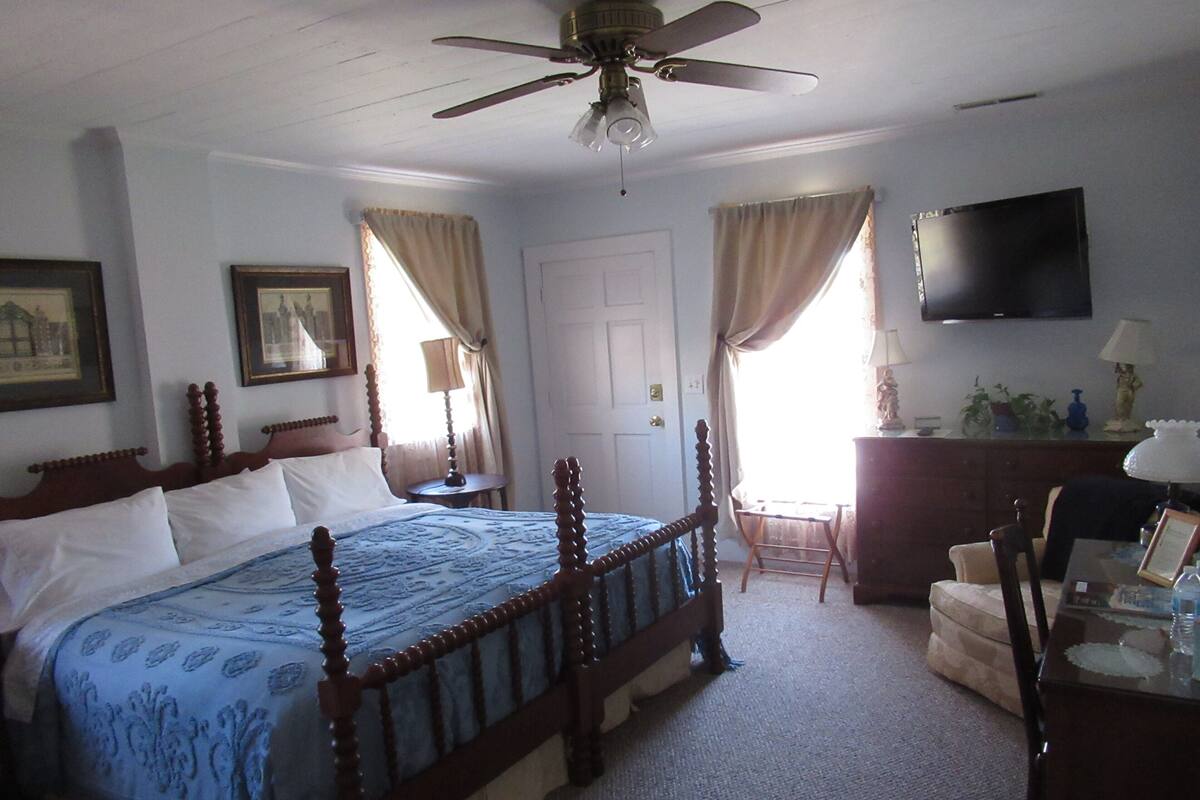 A bedroom with a wooden bed, a ceiling fan, a television, and a desk with a chair.