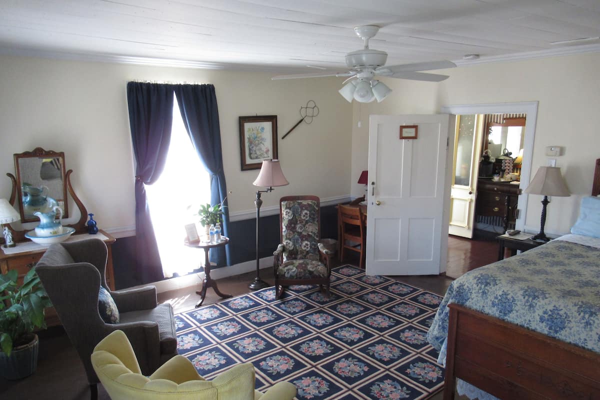 A bedroom with a bed, a chair, a desk, a lamp, a ceiling fan, and a door.