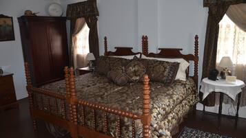 A traditional bedroom with a four-poster bed, a wooden wardrobe, and a small bedside table with a lamp.