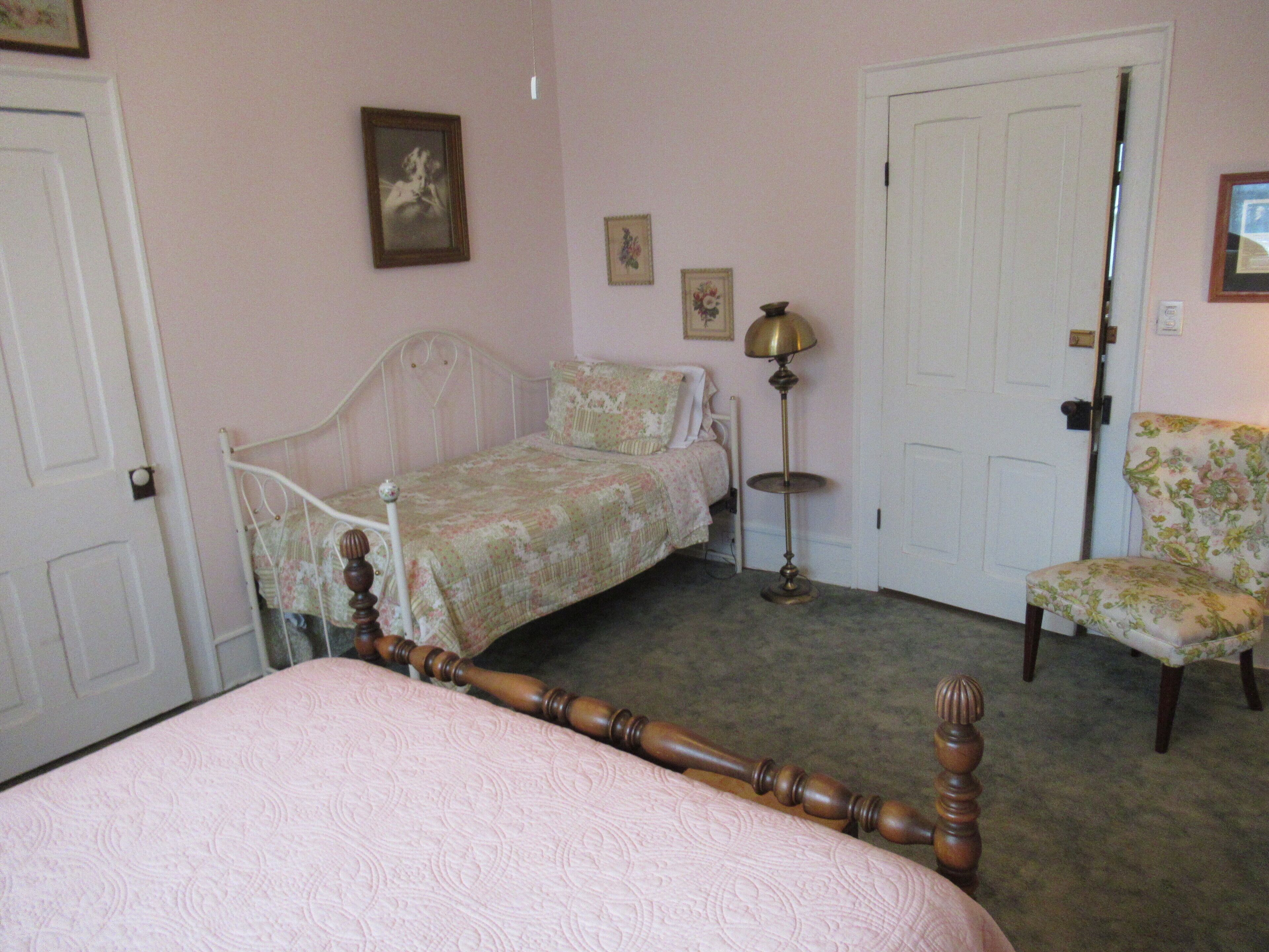 A bedroom with a bed, a chair, a bedside table, a lamp, and a door.