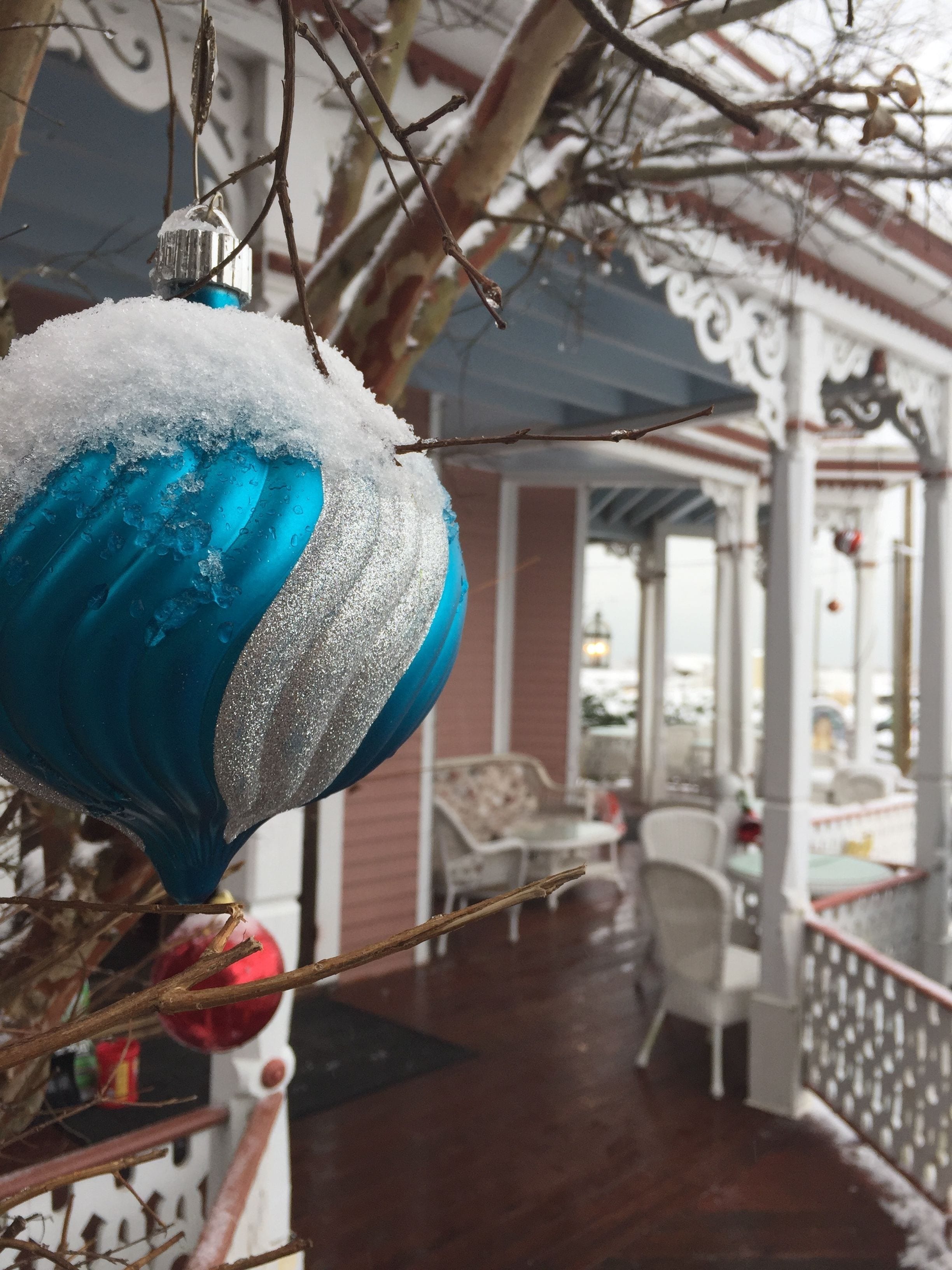 Un objet décoratif bleu recouvert de neige, des branches, une chaise blanche et une terrasse en bois.