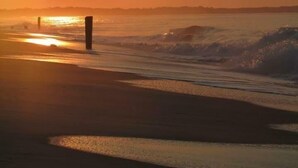 A sunset over a beach with waves and a clear sky.