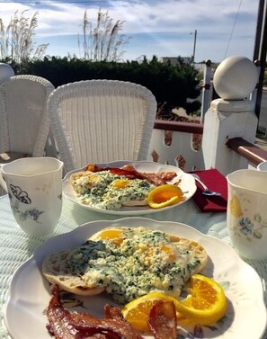 A table set with breakfast plates, including eggs and bacon, and two floral-patterned cups. - Angel of the Sea (Cape May)