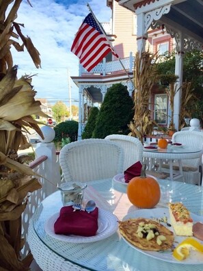 An outdoor dining area with white wicker furniture, a glass table, and a plate with food and a pumpkin.