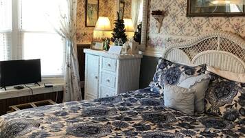 A bedroom with a large bed, a dresser, a television, and a window with curtains.