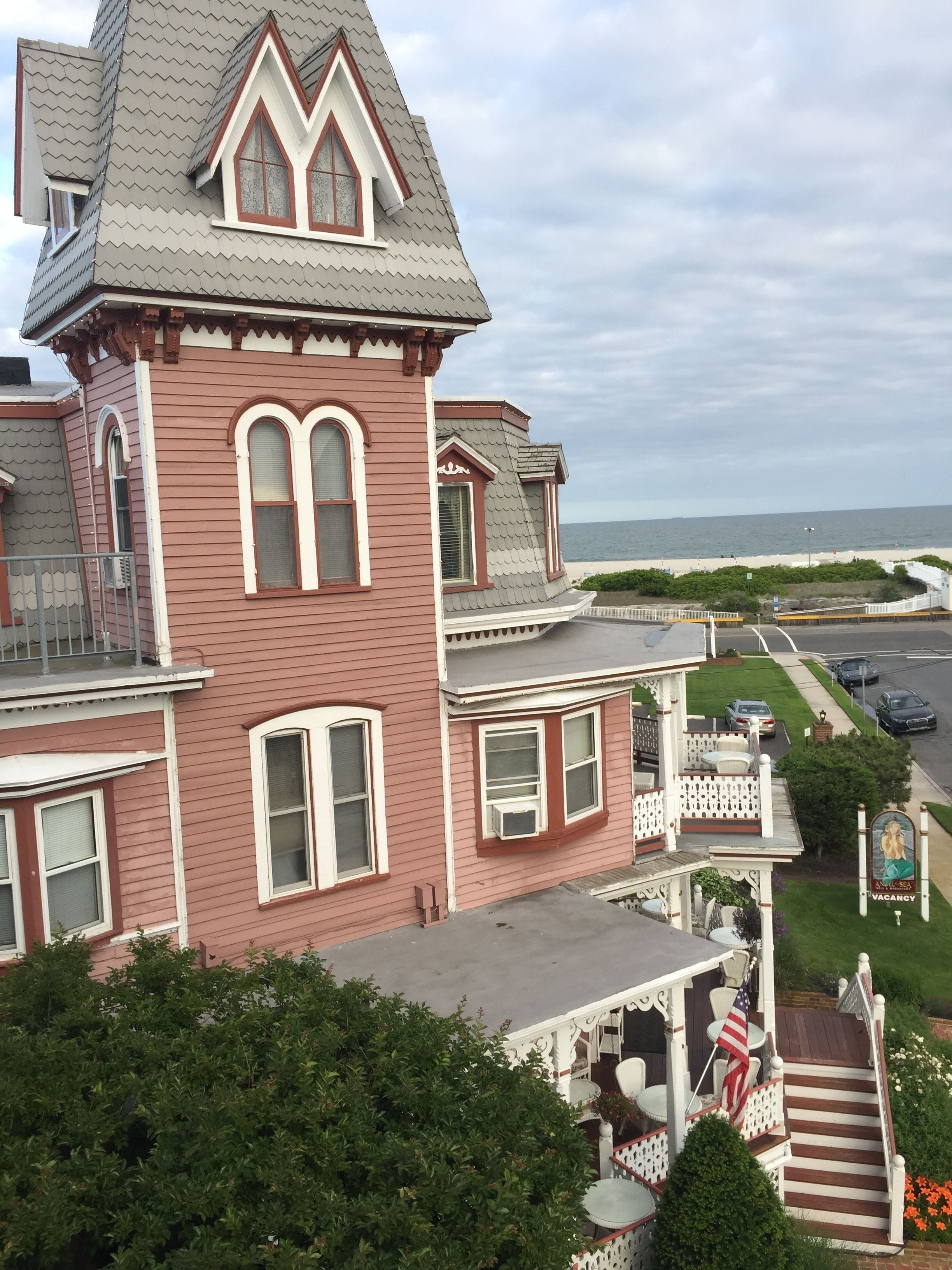 A Victorian-style house with a prominent tower, a porch with outdoor seating, and a view of the ocean.