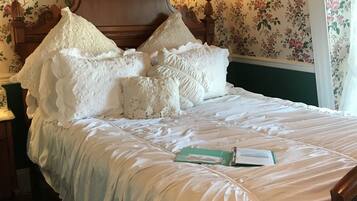 Una cama bien tendida con sábanas blancas y almohadillas de encaje, cabecera de madera y un libro verde sobre la cama.