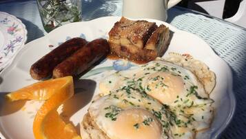 Une assiette avec des œufs, des saucisses, des toasts et une tranche d’orange.