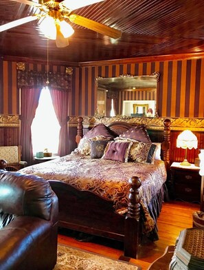 A traditional bedroom with a large bed, a wooden ceiling fan, a mirror, and a nightstand with a lamp. - Angel of the Sea (Cape May)