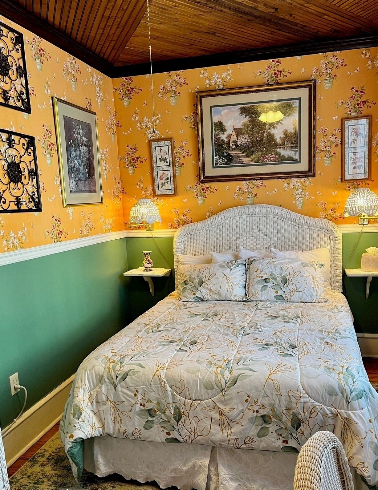 Een slaapkamer met een bloemenprint bedspreidek, groene wanden en meerdere ingelijste foto’s aan de muur.