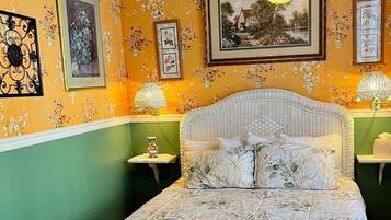 Un dormitorio con colcha de estampado floral, paredes verdes y varias fotografías enmarcadas en la pared.