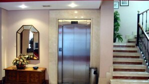 An elevator, a staircase, a trash bin, a mirror, and a wooden cabinet with a vase of flowers. - Doña Nieves (Norena)
