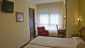 A hotel room with two beds, a TV, a framed picture, a red chair, a desk, and a window with curtains. - Doña Nieves (Norena)