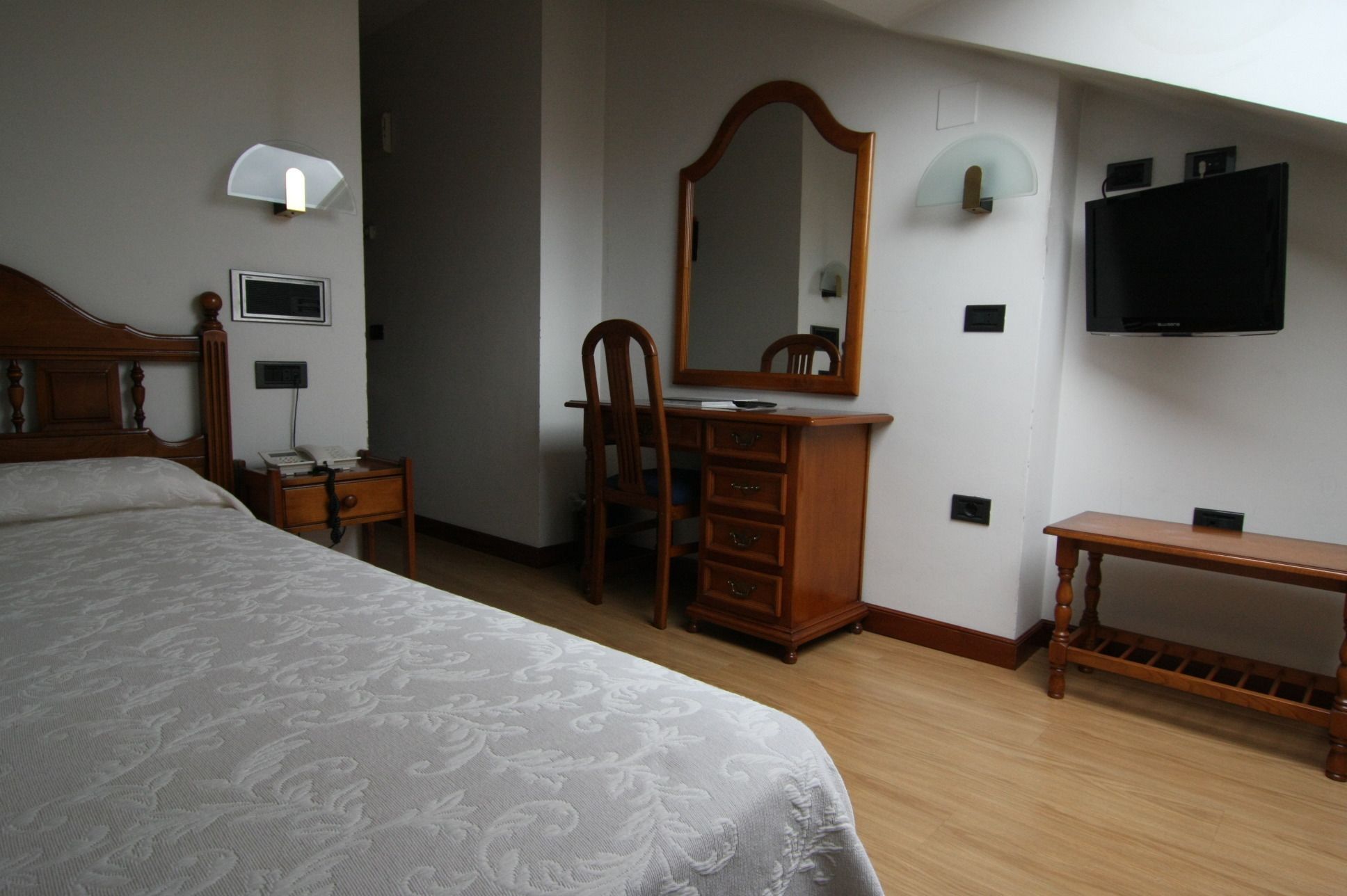 Un dormitorio con una cama grande, un aparador de madera, un espejo, un escritorio, una lámpara y un televisor montado en la pared.