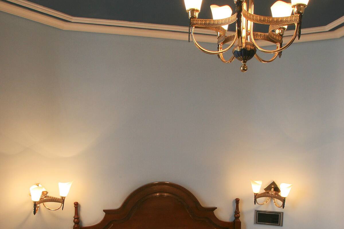 Un dormitorio con cama de madera, araña, lámparas de noche y mesita de noche.