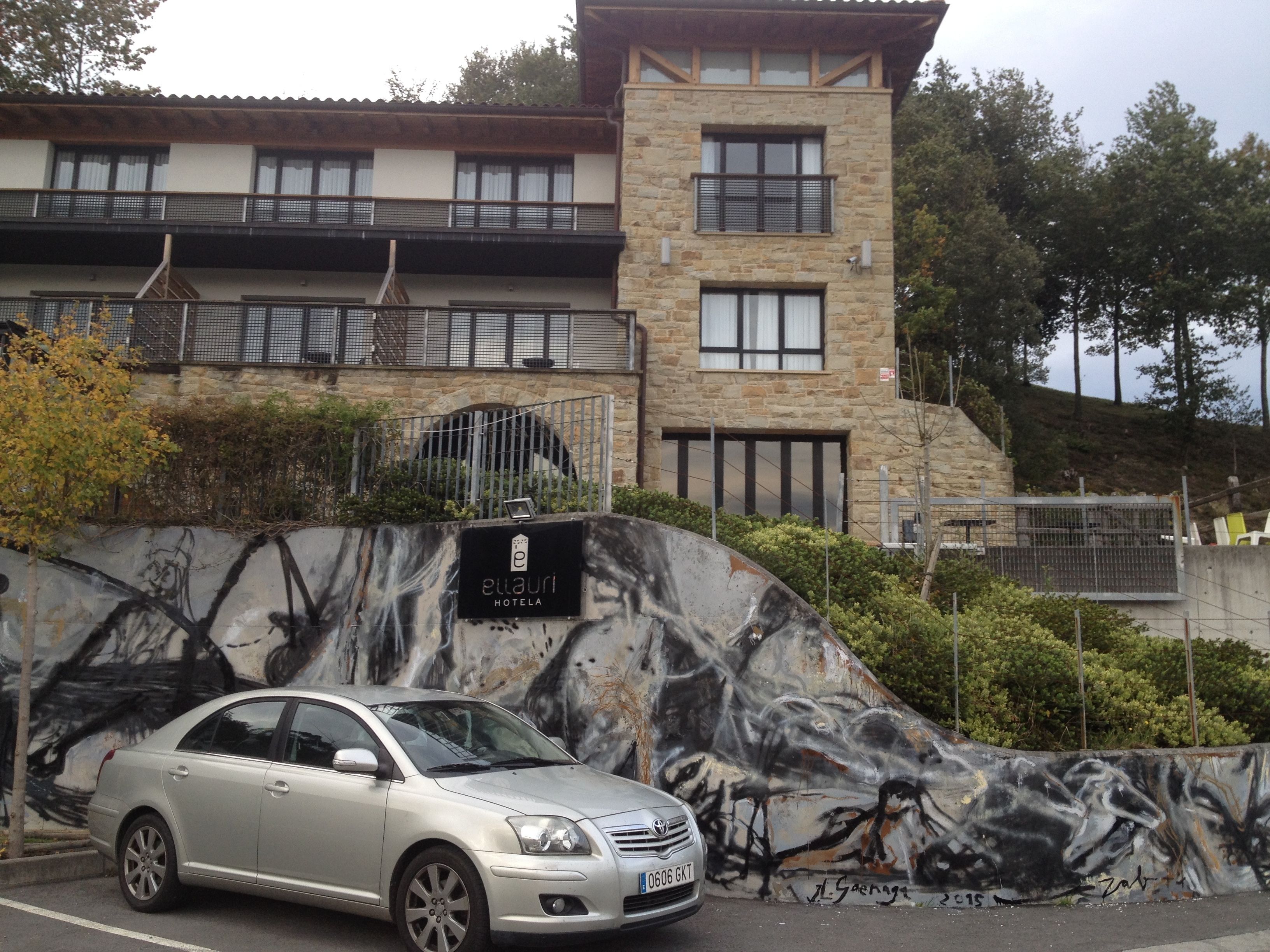 Un hotel de fachada de piedra, con un mural en la pared y un coche aparcado.