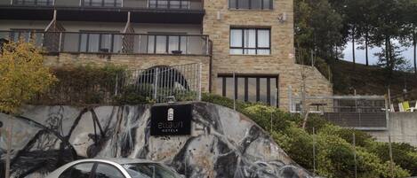 Un hotel de fachada de piedra, con un mural en la pared y un coche aparcado.