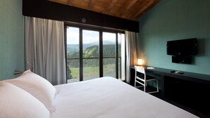 A hotel room with a large bed, a desk, a chair, a TV, and a view of a mountainous landscape through the window. - Ellauri Hotel, Landscape SPA - Adults Only (Zeanuri)