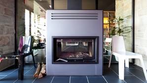A modern fireplace with a glass front, a white chair, and a stone wall. - Ellauri Hotel, Landscape SPA - Adults Only (Zeanuri)