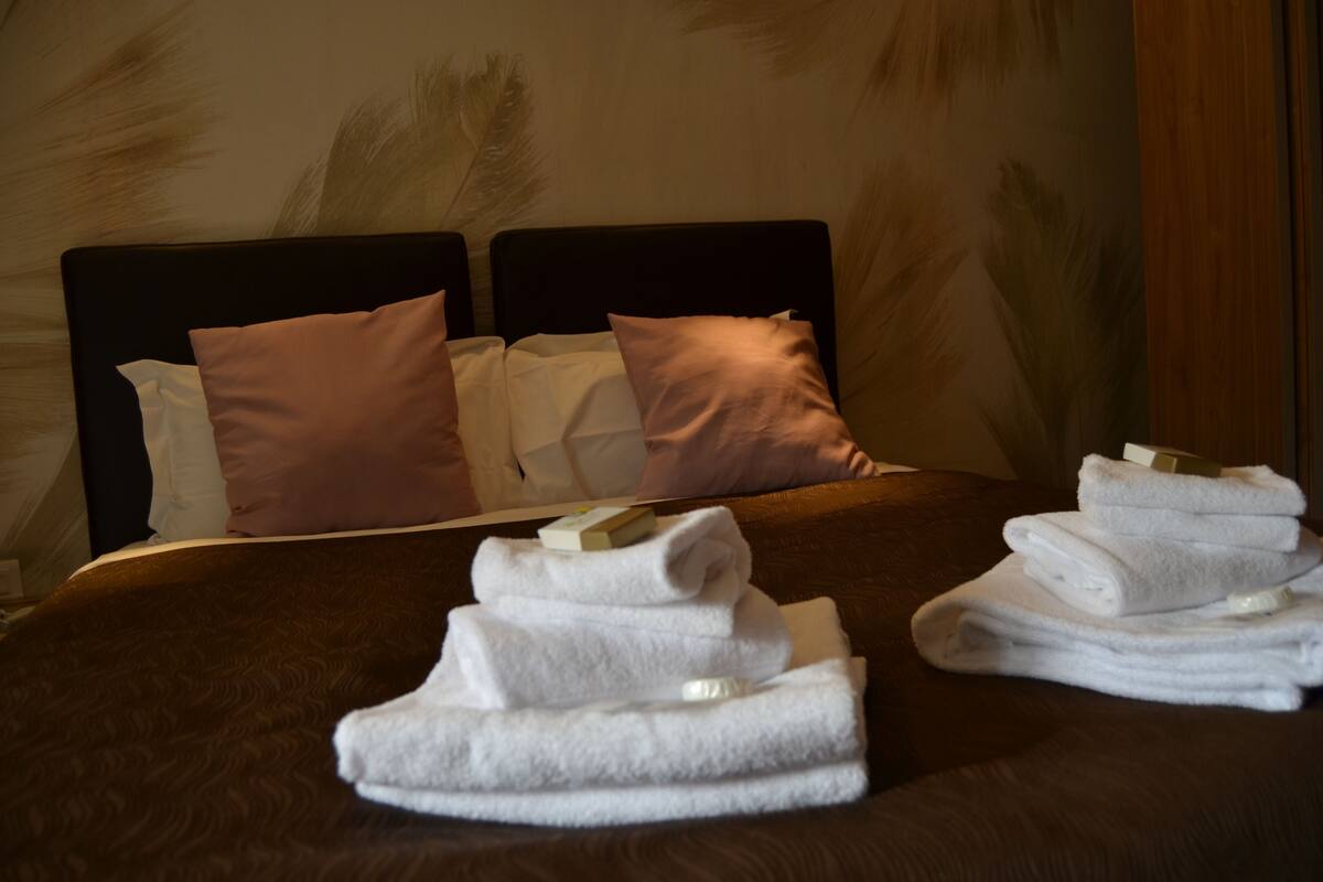 A neatly made bed with a brown bedspread, two pillows, and a stack of folded white towels.