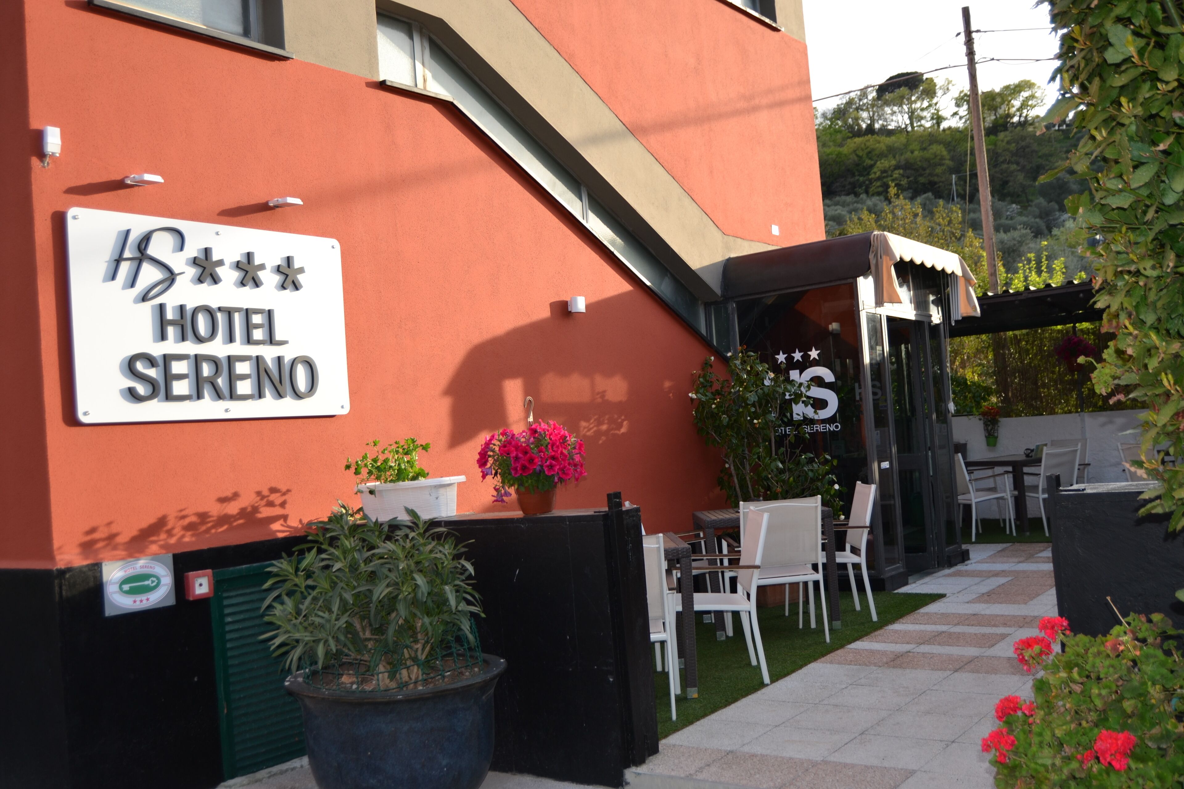A hotel exterior with a sign reading "HOTEL SERENO," outdoor seating, and potted plants.