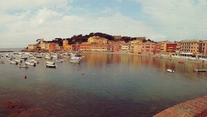 A coastal town with colorful buildings, a marina with numerous boats, and a prominent hill with a castle-like structure. - Hotel Sereno (Sestri Levante)
