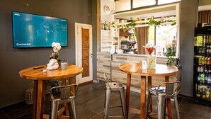 A restaurant with two wooden tables and metal chairs, a TV on the wall, and a kitchen area visible through an open door. - Hotel Sereno (Sestri Levante)