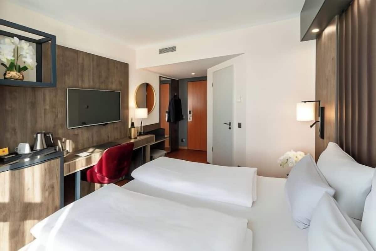 A hotel room with two beds, a desk, a chair, a TV, and a mirror.