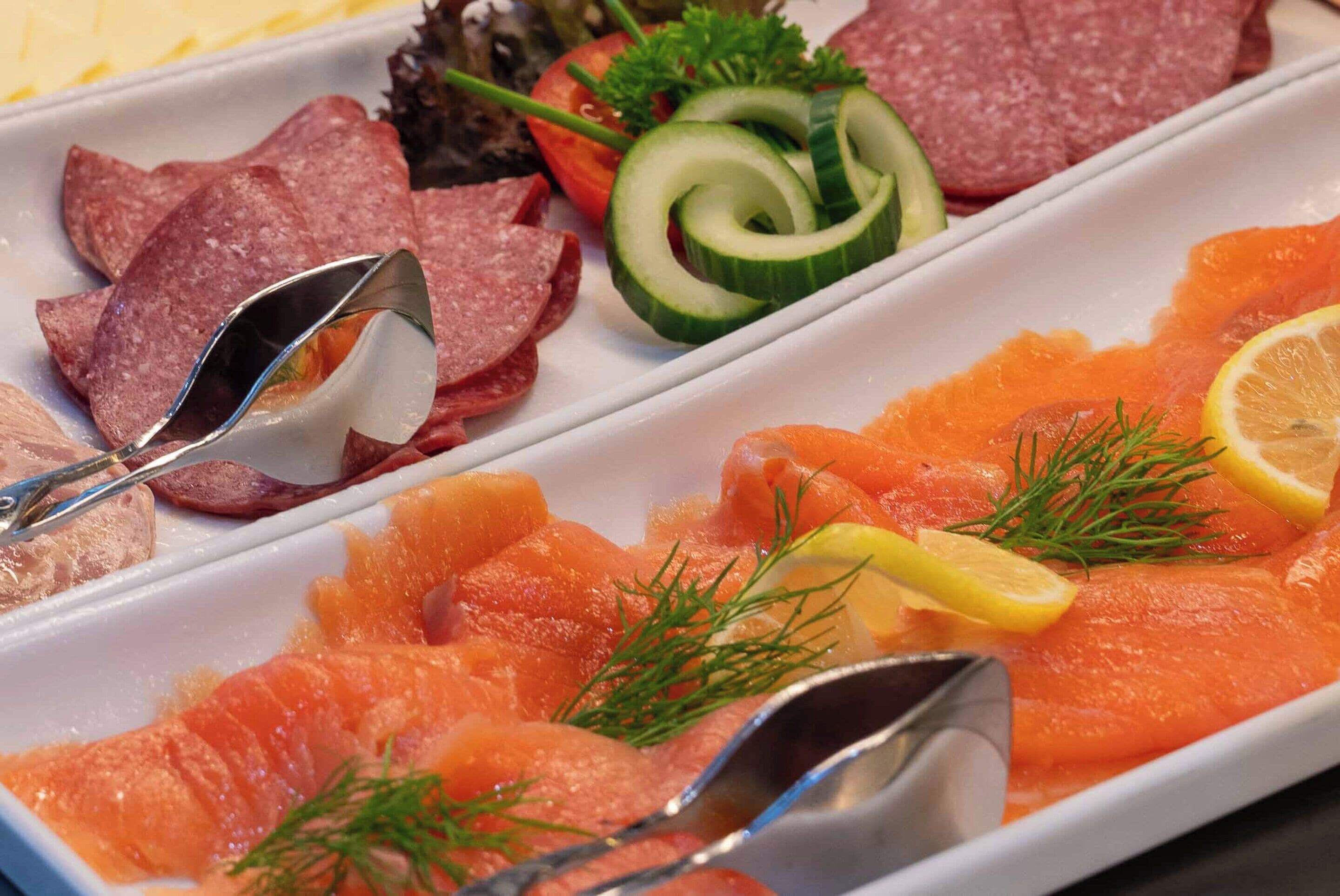 Una bandeja con varios tipos de carne y salmón ahumado, decorada con eneldo y rodajas de limón.