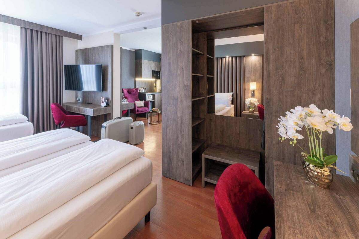 A hotel room with a large bed, a desk, a TV, a seating area, and a wardrobe.