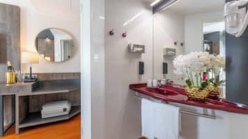 A modern bathroom with a vanity, a mirror, a red sink, and a towel hanging on the wall.