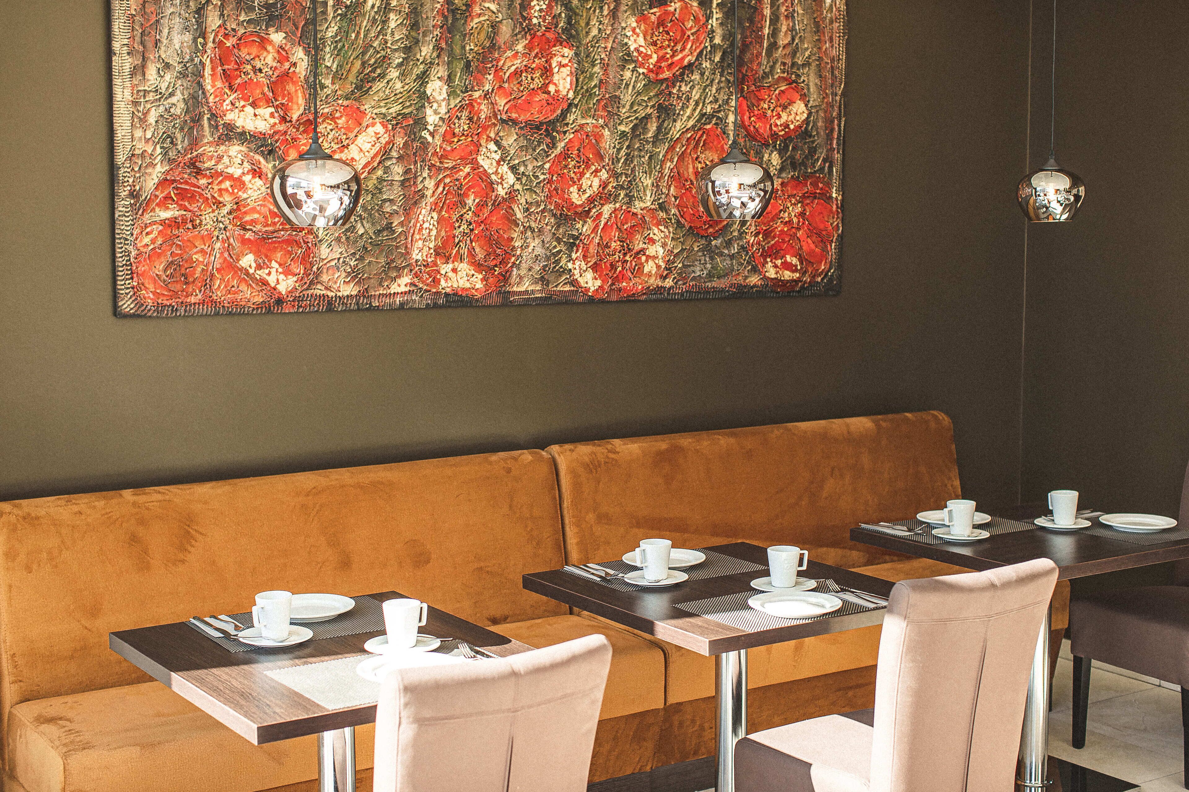 A restaurant with a brown cushioned bench seating, a table with a placemat, and a large floral artwork on the wall.