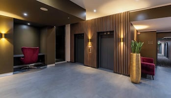 A modern lobby with a red chair, a large potted plant, and a wooden panel wall.