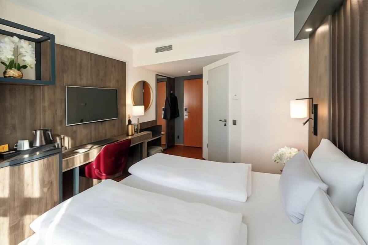 A hotel room with two beds, a desk with a chair, a TV, and a mirror.
